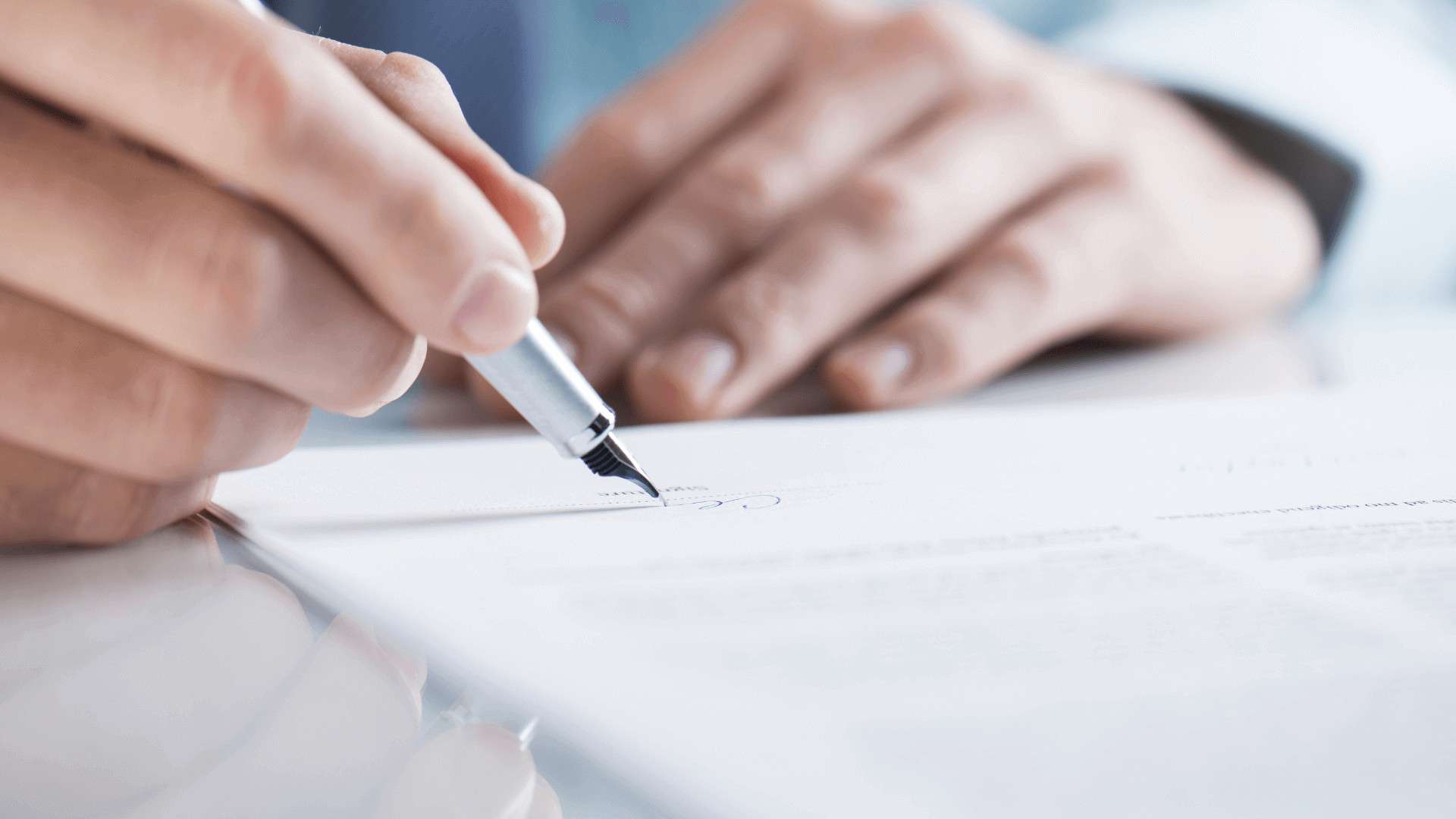 Eine Person, die mit einem Stift ein Dokument auf einem Tisch unterschreibt.